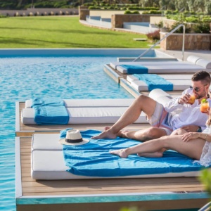 Guests enjoying a moment during their Kefalonia retreat with freshly prepared refreshment on the floating sunloungers at the pool of Electra Kefalonia Hotel & Spa.