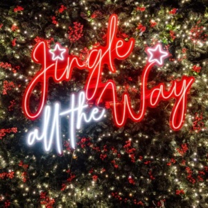 The neon "Jingle All the Way" sign frames the joyful atmosphere at Electra Hotels, perfect for celebrating festive getaways to Athens, Greece.
