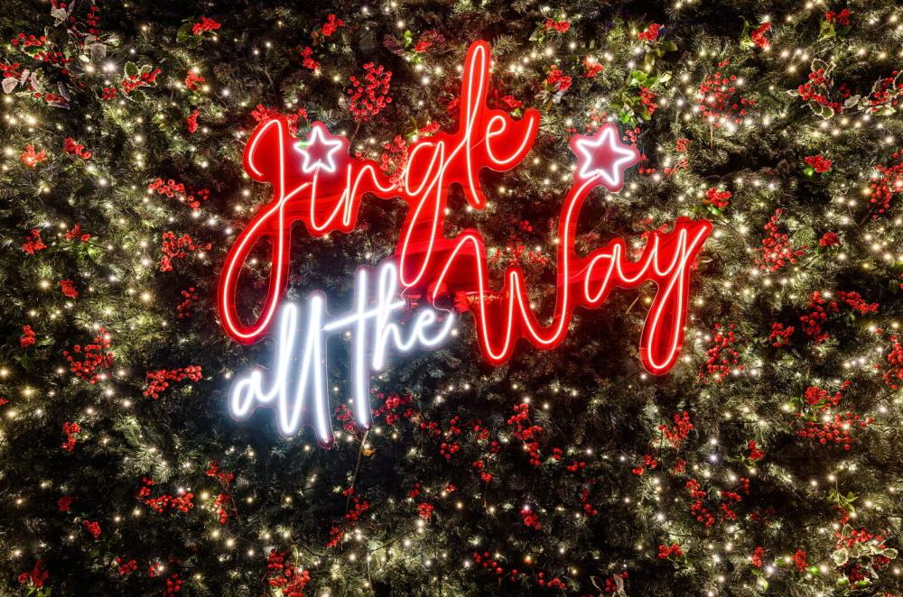 The neon "Jingle All the Way" sign frames the joyful atmosphere at Electra Hotels, perfect for celebrating festive getaways to Athens, Greece.